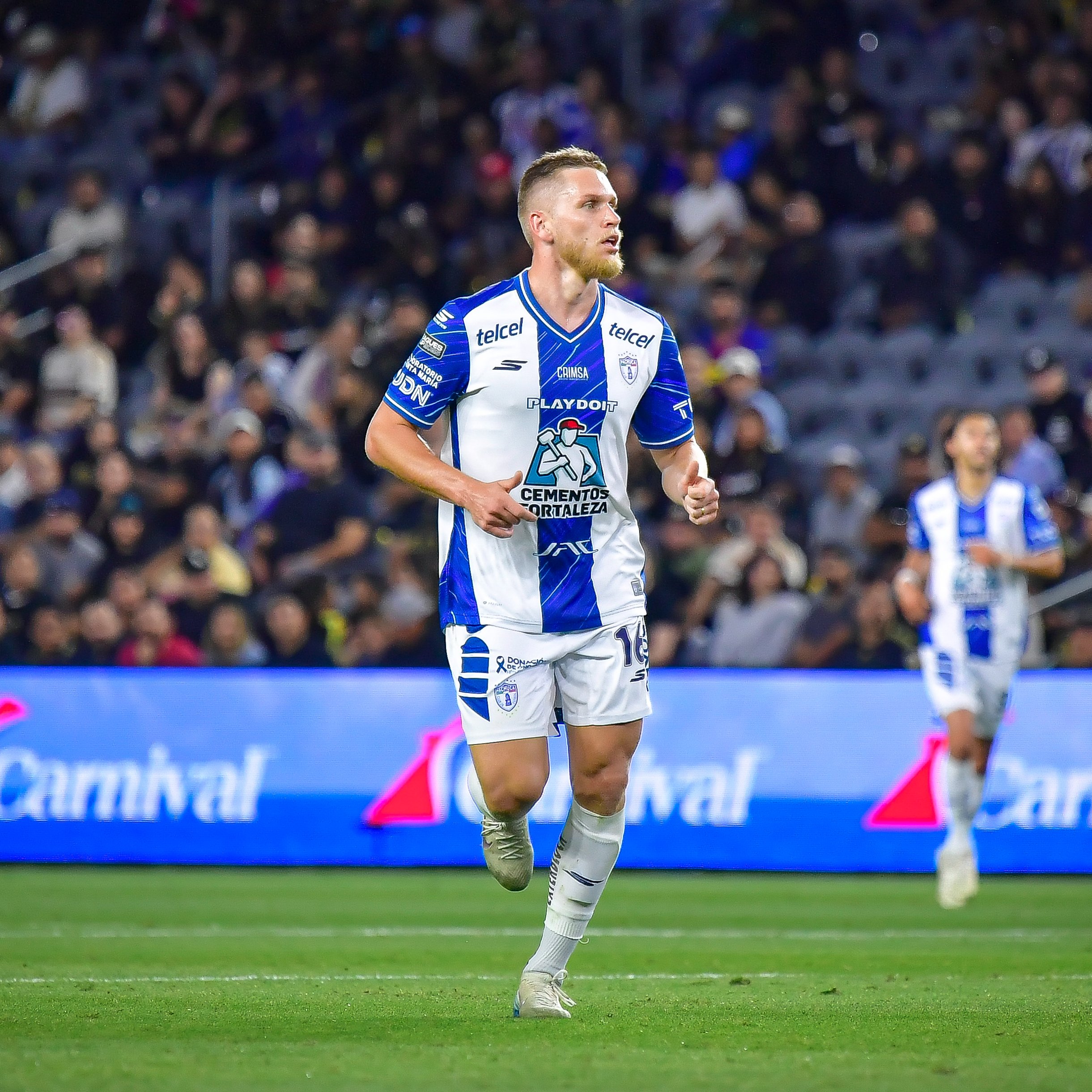 Soccer player in a blue-and-white kit running on a field with a packed stadium in the background.