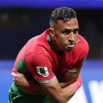 726606909_1533526261487393_5645636091625464398_n | The Soccer Goal Soccer player in red jersey and green shorts bending forward, balancing on one leg during a match on a green field.",